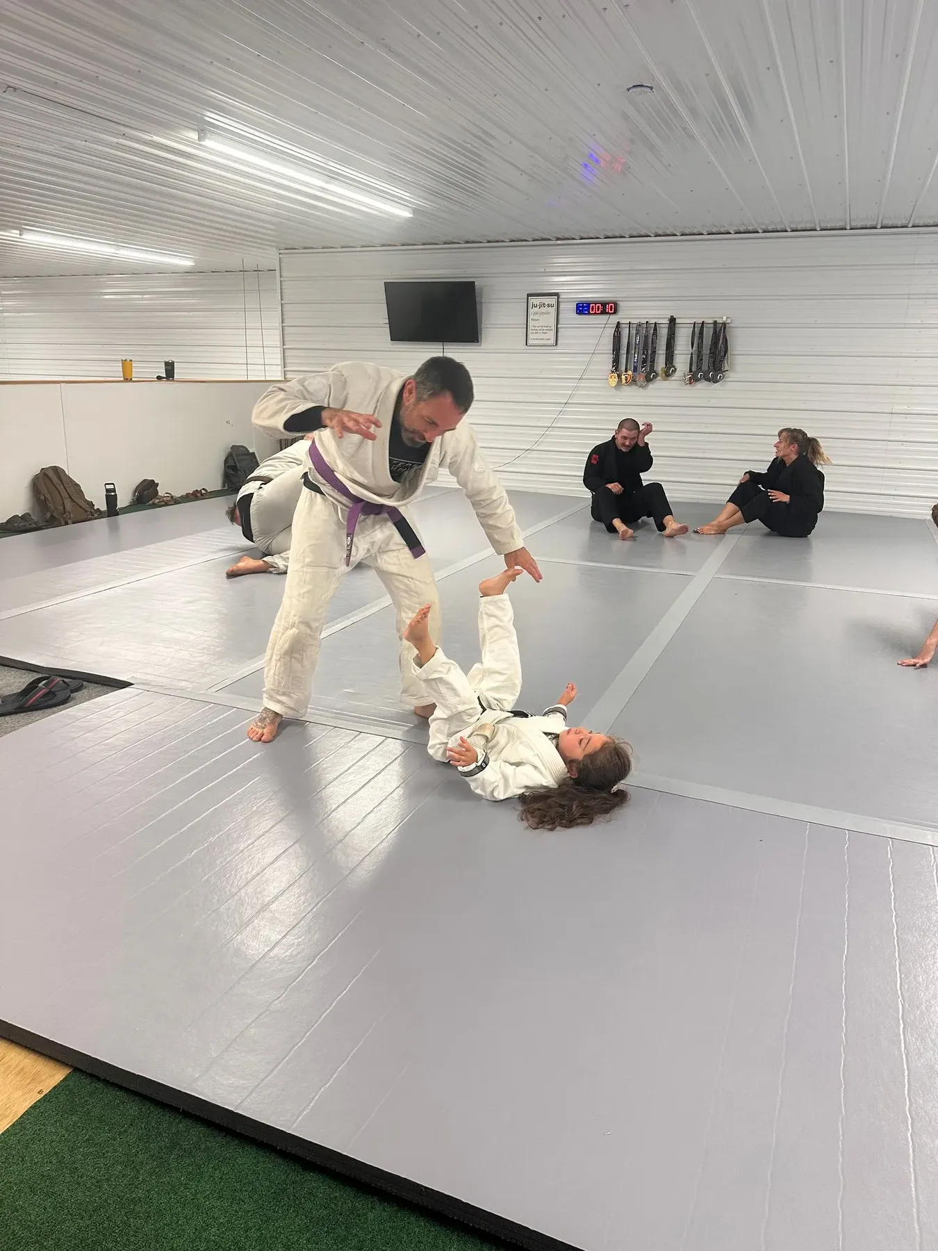 An instructor teaches a young student a leg position while other students watch.
